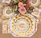 A fall-themed table setting features the Turkey & Gourds Table Setting Bundle by Sophistiplate LLC, including designer disposable plates adorned with turkey and gourd motifs, gold cutlery, plaid and burlap placemats, and a floral centerpiece with pink roses and autumnal blooms. The distinctive turkey design appears on both the top plate and matching napkin.
